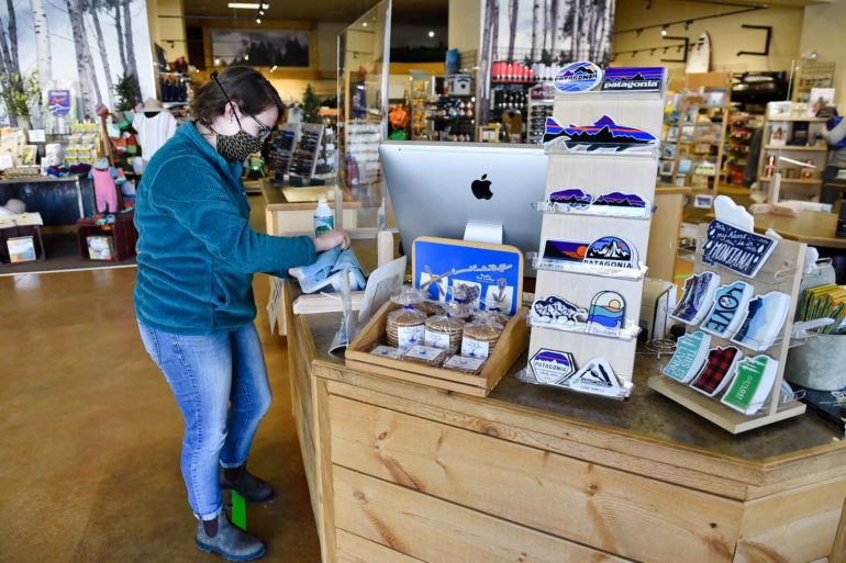 Bella Summers disinfects the cashier stand at The Base Camp in Helena, Montana, on the business’s first day open since the lifting of some coronavirus-related closures. (AP Photo, Thom Bridge)