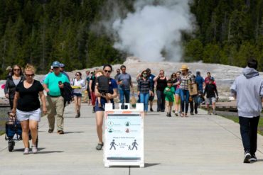 Visitors walk away from Old Faithful as a sign about COVID-19 safety sits in the sidewalk in Yellowstone National Park after reopening in 2020. (AP Photo, Ryan Berry)