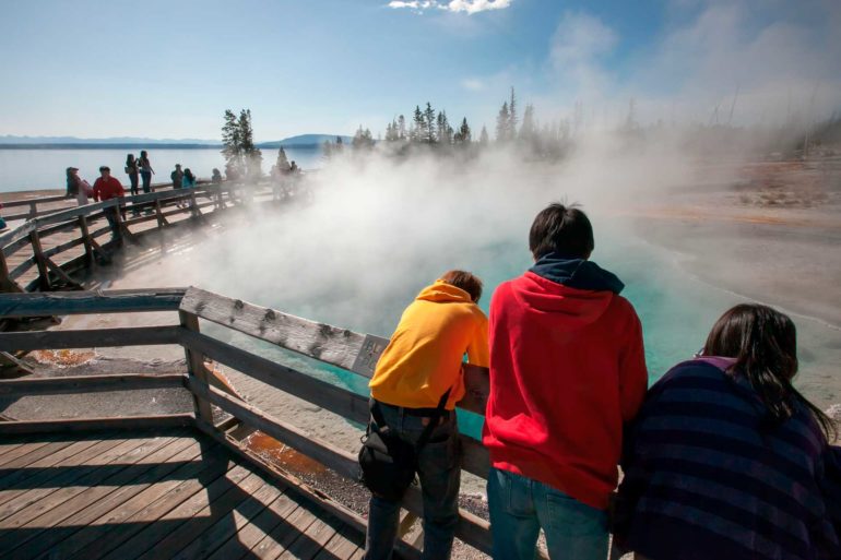 Tourists lean over a railing to observe geothermal features in Yellowstone National Park. (Design Pics, AP Photo)